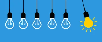 A row of hanging light bulbs, with one glowing yellow bulb standing out among the unlit bulbs against a blue background.